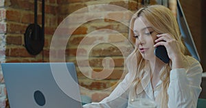 A focused woman is using her laptop computer while talking on the phone sitting in the cafe.