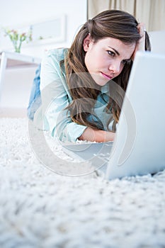 Focused woman using her laptop lying on the floor