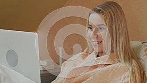 Focused woman using laptop having video chat while lying in hospital bed