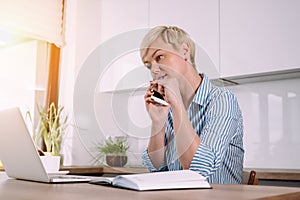 Focused Woman working on laptop at home talking on phone and making notes Female using portable computer.