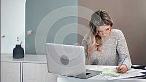 Focused woman writing paperwork e learning use laptop pc in home office. Medium shot on RED camera