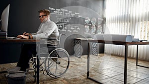 Focused at work. Side view of young male designer in a wheelchair using stylus pen and digital tablet while sitting at