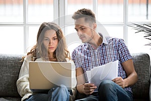 Focused worried couple paying bills online on laptop with document photo