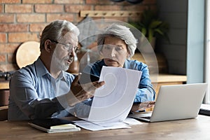 Focused worried older spouses reading financial documents checking bills