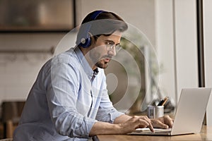 Focused young 30s businessman in headphones using computer.