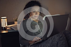 Focused black female student with curly short hair taking an online classes on laptop and looking at screen. Indoors at home photo