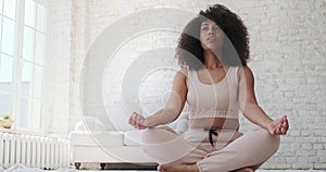 Focused young black woamn sits mat, legs crossed, doing yoga breathing exercise.