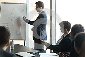 Focused young business trainer explaining hand drawn charts on whiteboard.