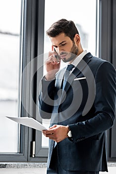 focused young businessman holding papers and talking on smartphone