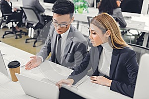 Focused young businesspeople discussing work and pointing at laptop