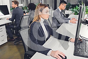 Focused young businesswoman using desktop computer while working with colleagues