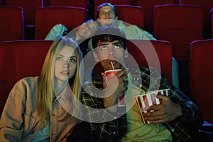 Focused young couple, attractive man and woman really interested in watching film while sitting at the cinema, eating