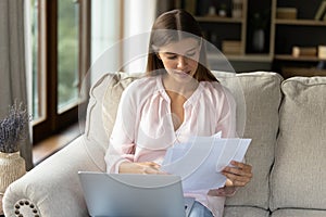 Focused young female homeowner studying paper bills