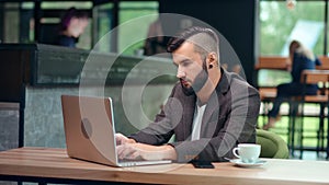 Focused young freelancer man with trendy hairstyle working on laptop pc sitting at public cafe place
