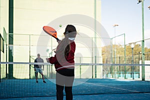 A focused young girl practices her paddle tennis skills on a vibrant blue court on a clear day