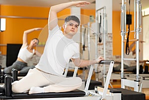 Guy doing side bend with arm extended on Pilates reformer photo