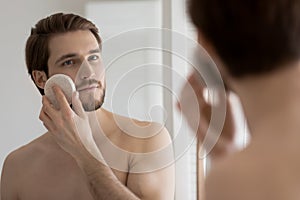 Focused young handsome guy using cellulose sponge.