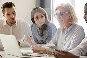 Focused young interns making notes listening to old female manager photo