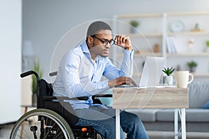 Focused young man in wheelchair using laptop computer for online work or communication at home