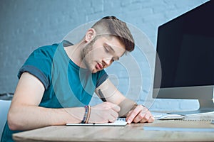 focused young man writing in notebook while working