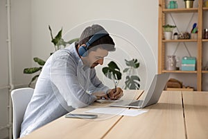 Focused young student guy in earphones watching virtual class