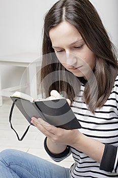 Focused young student takes notes in notebook using pencil, sitting on white wooden floor