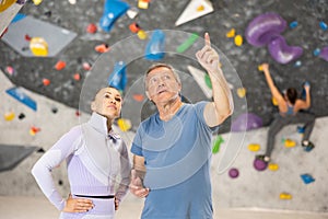 Focused young woman and elderly man talking in climbing gym