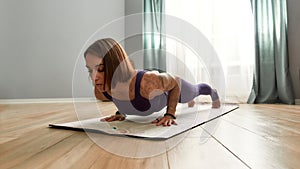 Focused young woman exercising, doing Four Limbed Staff yoga pose on a mat in living room at home on a daytime