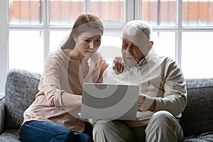 Focused young woman helping older daddy with computer applications.