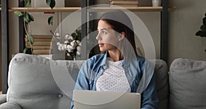 Focused young woman sit on couch work on laptop