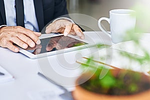 Focusing his efforts on getting the job done. a corporate businessman working on a digital tablet in an office.