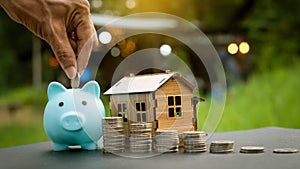 Focusing on the piggy bank, the man puts coins into the piggy bank, where the coin and house are personal finance backgrounds,