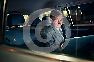 Focusing on work- businessman working on his laptop on the back seat of the car