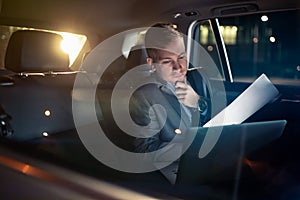 Focusing on work- businessman working on his laptop and paper on the back seat of the car