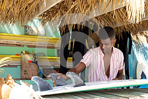 Focussed african american man preparing surfboard behind counter of surf hire beach shack