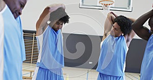 Focussed diverse male basketball players stretching arms at training session, slow motion