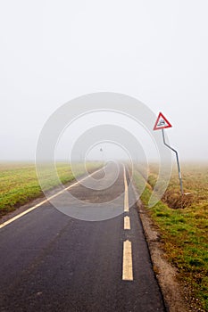 Fog along empty rural road with danger sign