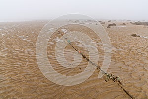 Fog lifting over an endless wadden sea beach at low tide with a mooring rope for boats in the foreground
