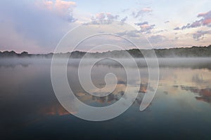 Fog lifts off the lake with dramatic cloudscape at sunrise