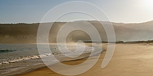 Fog and mist rising from a golden sand beach with gentle lapping waves