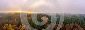 Fog over a autumn colored forest at the autumn season, a panoramic mystical view at the sunset shot by a drone.