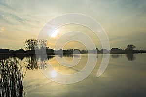 Fog over lake and sun behind clouds before sunset