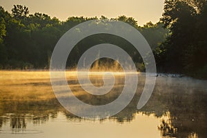 fog over the river in the early morning illuminated by the sun, the reflection of trees