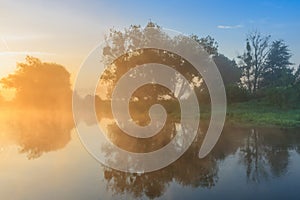 Fog over river surface in orange sunrise. River landscape in summer morning