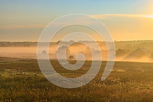 Fog over village houses in orange rays of rising sun in autumn morning. Nature landscape