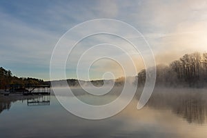 Fog rises by a dock on the surface of the water at sunrise in winter on Lake Lanier in Georgia, USA photo