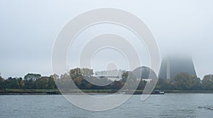 Foggy autumn morning in Germany on the river Rhine, a flowing barge. Visible chimney of a nuclear power plant in the fog.