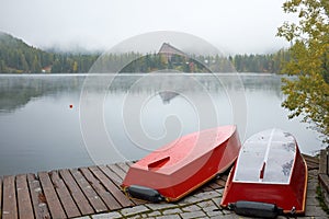 The foggy autumn Strbske Pleso lake with boats on the pier