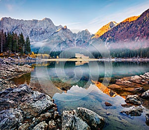 Foggy autumn view of Fusine lake. Picturesque morning scene of Julian Alps with Mangart peak on background, Province of Udine, Ita