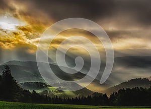 Foggy epic glorious sunrise over a countryside with hills,fields, trees,dramatic sky